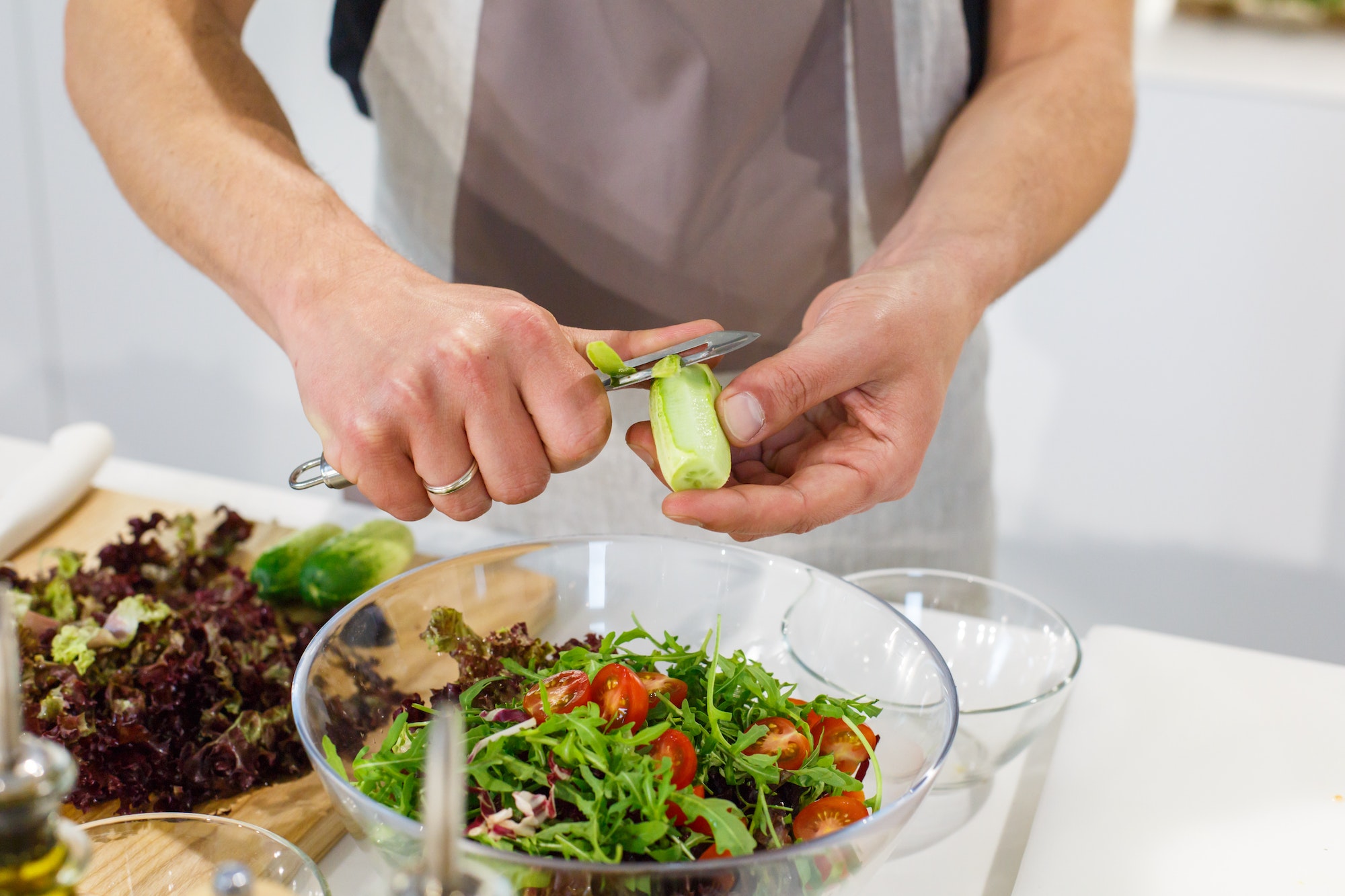Chef cutting cucumber for healthy salad in light kitchen.