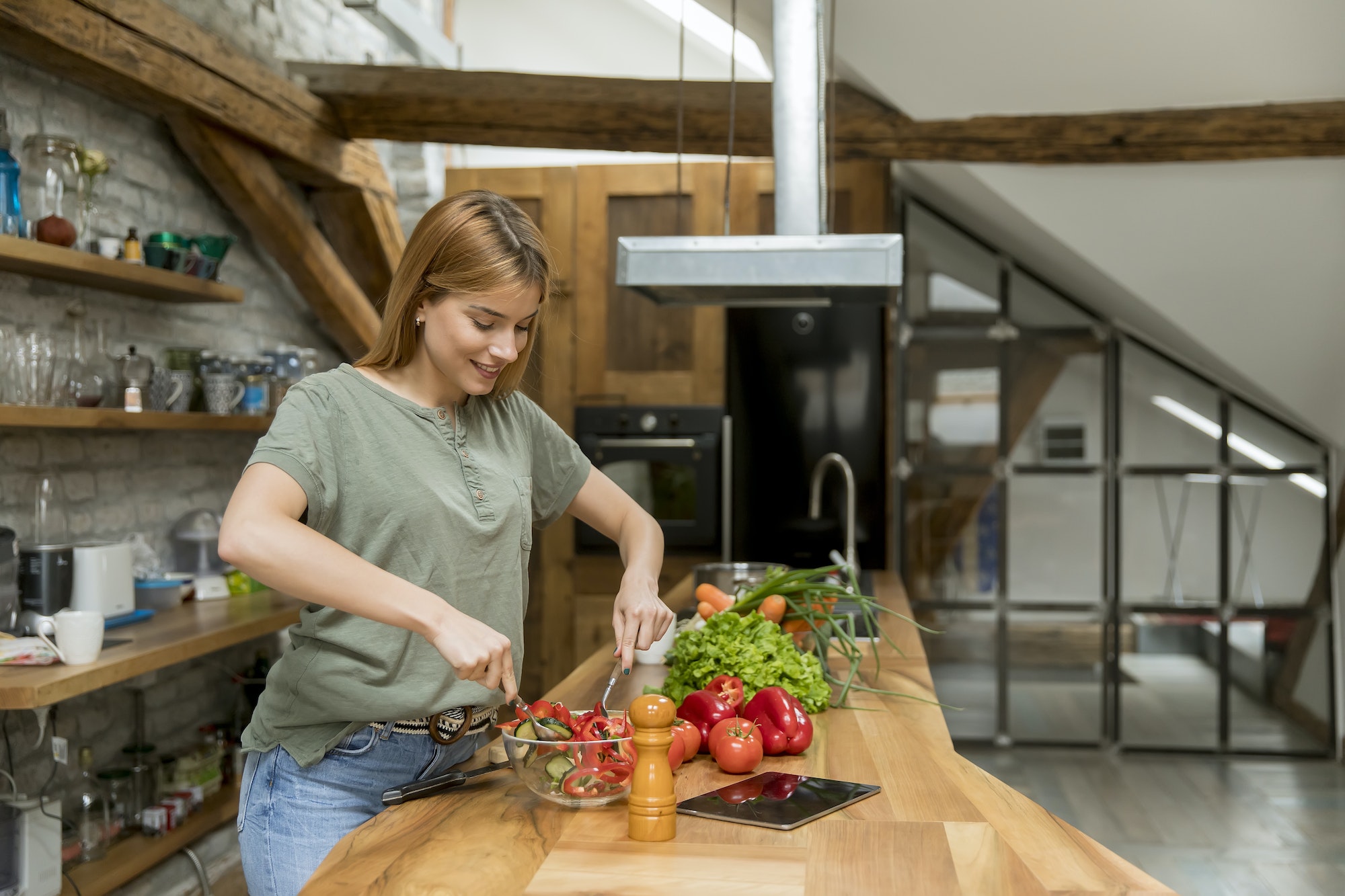 Happy young woman cooking delicious and healthy food in the loft kitchen at home