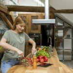Happy young woman cooking delicious and healthy food in the loft kitchen at home
